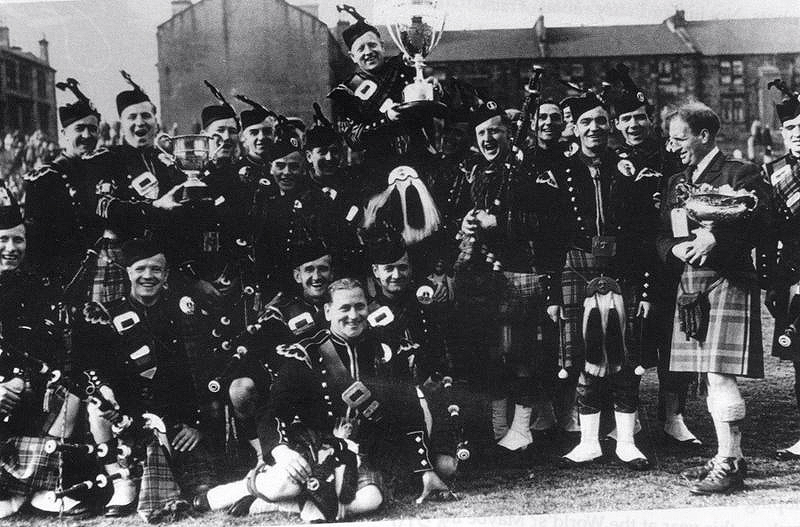 The victorious Shotts & Dykehead Pipe Band in 1959 with P/M John MacAllister held aloft with the trophy. Also in picture are Alex Duthart (left with trophy) and piper John Finlay (rear right standing). Can anyone put names to the other individuals pictured? If so please email pipingpress@gmail.com