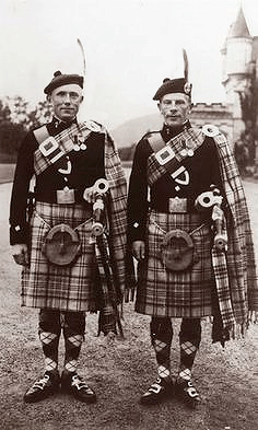 RB Nicol and RU Brown in their heyday as King's Pipers. They are wearing the Balmoral tartan and the turrets of the castle can be seen in the background